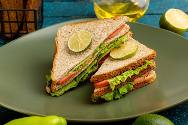 leckeres Sandwich mit grünen Salattomaten und Schinken in Teller auf blau