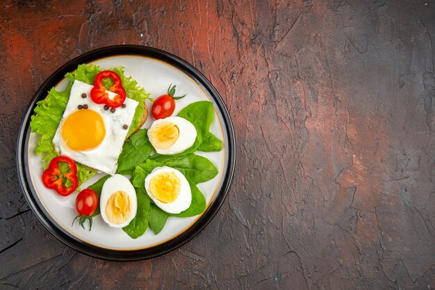 Leckeres Sandwich von oben mit Rührei und gekochten Eiern und Salat im Teller auf dunklem Tisch