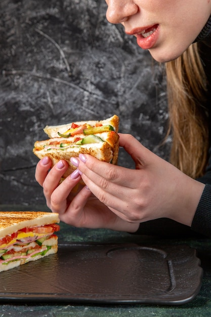 Leckeres Schinkensandwich der Vorderansicht, das von Frau auf dunkler Oberfläche gegessen wird