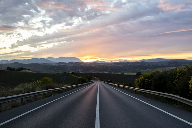 Leere Autobahn, umgeben von Hügeln unter dem bewölkten Sonnenuntergangshimmel