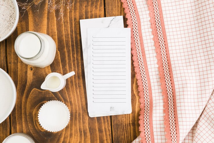 Kostenlose Foto leere liste auf notizblock mit milchglas- und schalenkuchenform über hölzernem schreibtisch nahe tischdecke