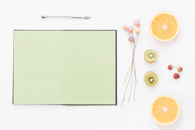 Leere Seite Notizbuch; Stift; getrocknete Blume; Erdbeere und halbierte Früchte auf weißem Hintergrund