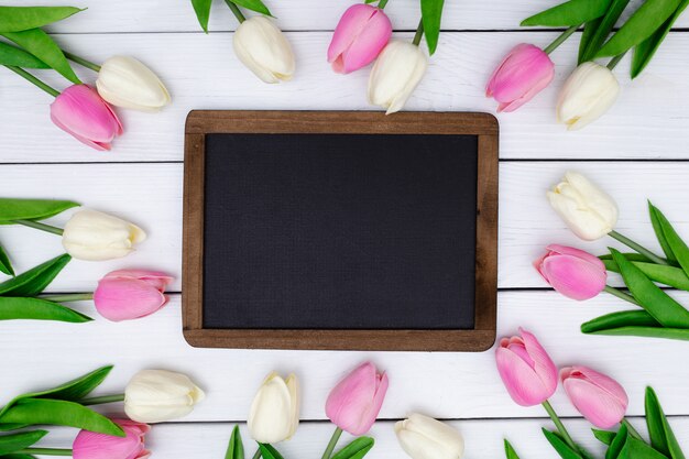 Leere Tafel mit einer Frühlingszusammensetzung mit Tulpen auf weißem hölzernem