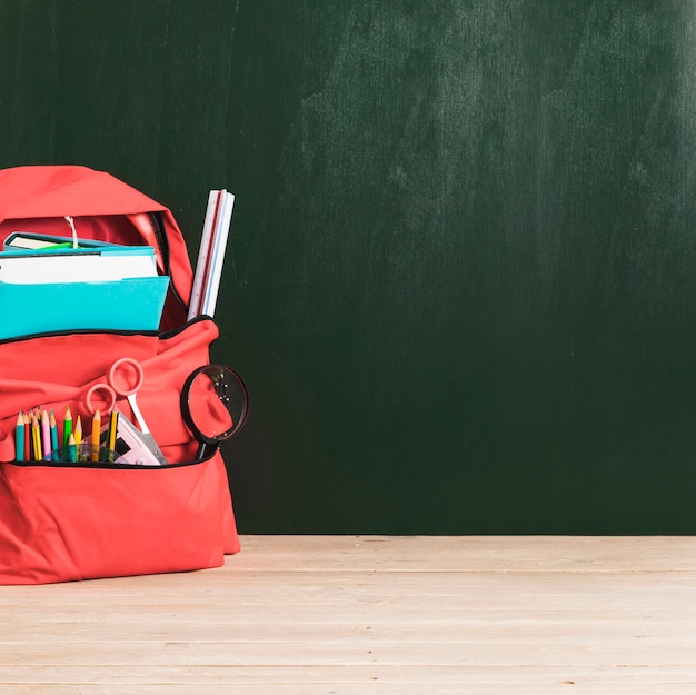 Leere Tafel und roter Schulrucksack mit Versorgungen