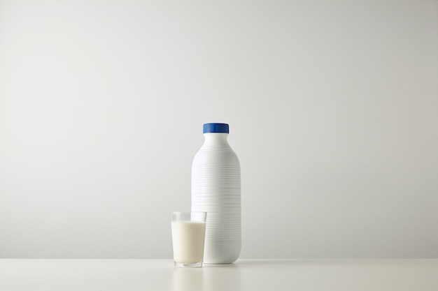 Leere weiße Plastikflasche mit blauer Kappe nahe Glas mit Milch lokalisiert auf weißer Tischmitte, reiche Textur