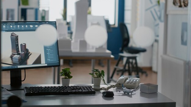 Leerer architektonischer Arbeitsplatz mit Gebäudemodell und 3D-Bauplan auf dem Tisch. Niemand im Büro mit Computer und Werkzeugen für Stadtentwicklung und Architekturdesign.