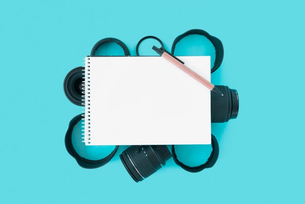 Leerer gewundener Notizblock mit Stift über Kamerazubehör auf blauem Hintergrund