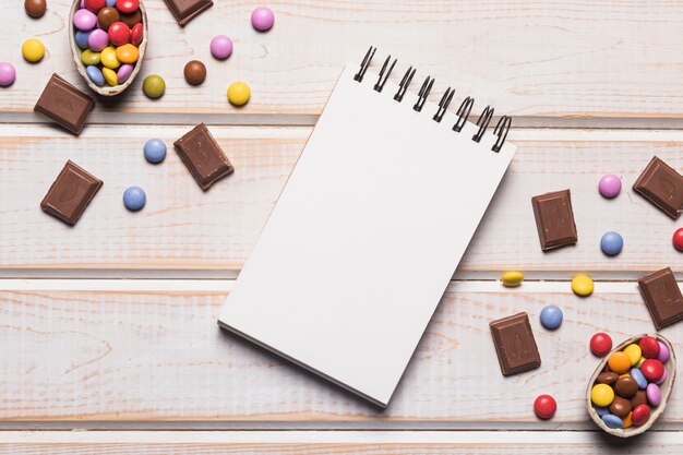 Leerer gewundener Notizblock zwischen den Edelsteinen und Schokoladenstücken auf hölzernem Schreibtisch