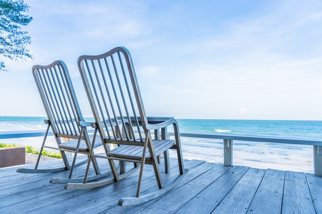 Leerer hölzerner Stuhl und Tabelle am Patio am im Freien mit schönem tropischem Strand und Meer