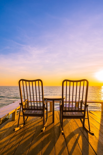 Leerer hölzerner Stuhl und Tabelle am Patio am im Freien mit schönem tropischem Strand und Meer