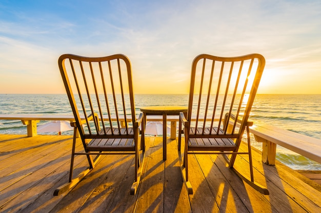 Leerer hölzerner Stuhl und Tabelle am Patio am im Freien mit schönem tropischem Strand und Meer