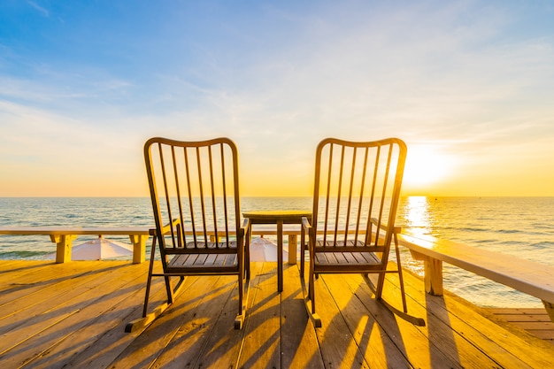 Leerer hölzerner Stuhl und Tabelle am Patio am im Freien mit schönem tropischem Strand und Meer