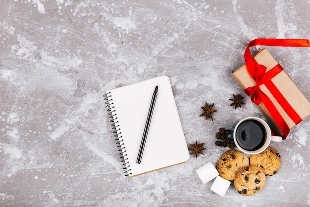 Leerer notebbok liegt vor Tasse Kaffee, Präsentkarton und köstlichen Plätzchen