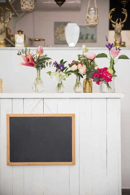 Leerer Schiefer, der an der Wand mit schönen Blumenvasen im Blumenladen hängt