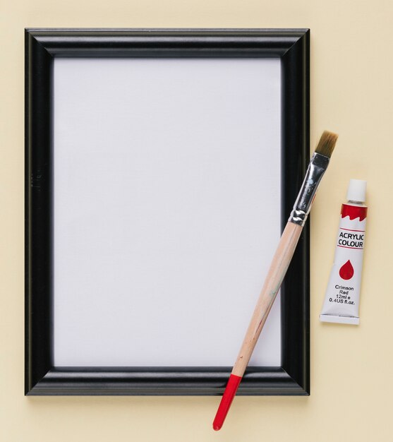 Leerer weißer Bilderrahmen mit Lackgefäß und Malerpinsel