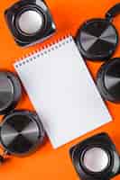 Kostenloses Foto leerer weißer gewundener notizblock mit kopfhörer und sprecher auf einem orange hintergrund
