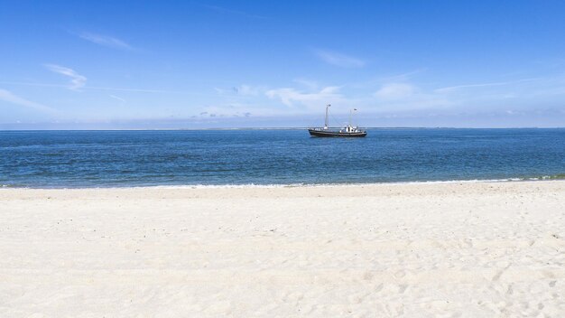 Leerer weißer Sandstrand mit einem auf dem Wasser schwimmenden Schiff