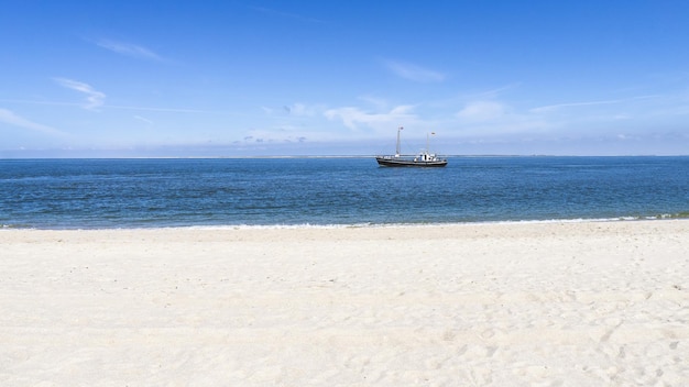 Leerer weißer Sandstrand mit einem auf dem Wasser schwimmenden Schiff