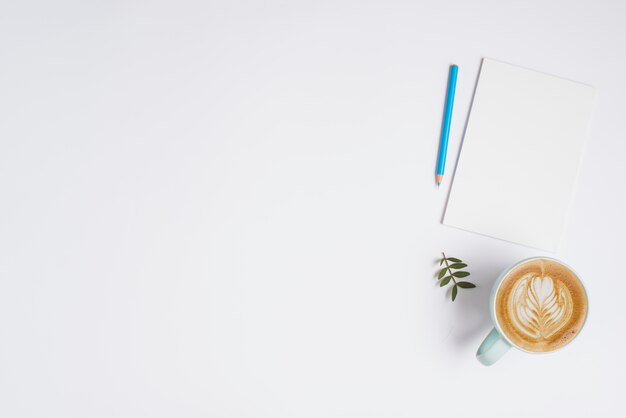 Leeres Blatt; Blauer farbiger Bleistift und Cup Cappuccino auf weißem Hintergrund