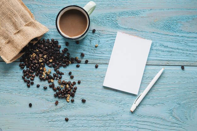 Leeres Blatt; Stift mit Tasse Kaffee und Kaffeebohnen auf blauem strukturiertem Tisch