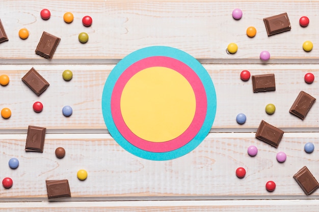 Leeres Blau; rosa und gelber Kreisrahmen mit Süßigkeiten auf hölzernem Schreibtisch