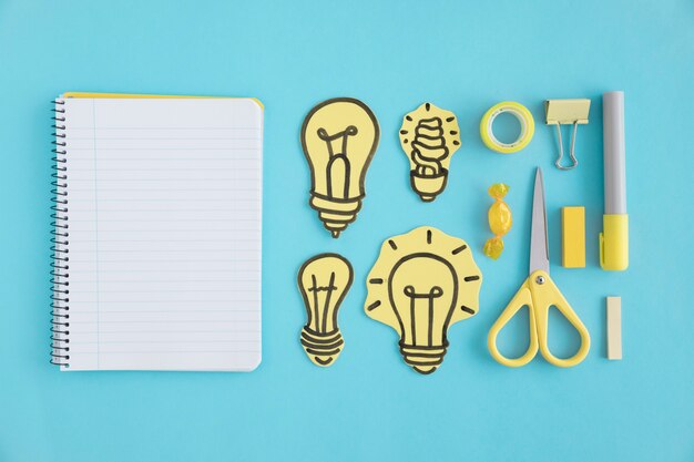 Leeres gewundenes Notizbuch mit Papierglühlampen und -briefpapier auf blauem Hintergrund