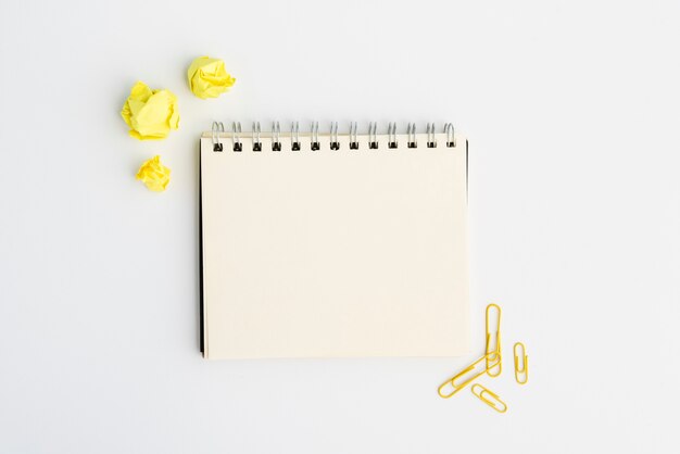 Leeres gewundenes Tagebuch mit Gelb zerknittertem Papier und Papierklammer über weißem Hintergrund