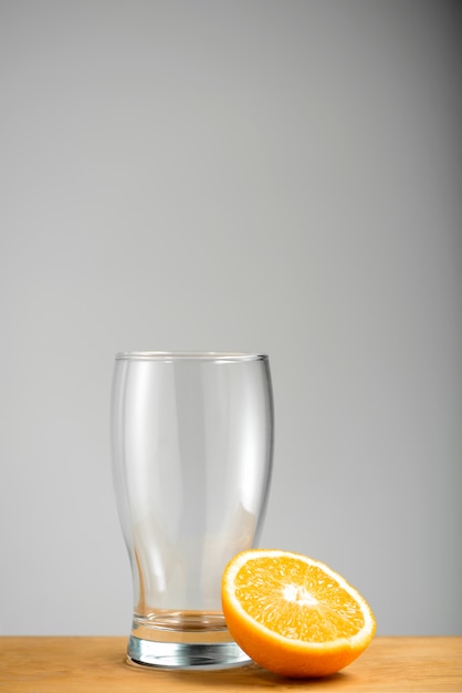 Kostenloses Foto leeres glas mit halber orange auf holzschreibtisch