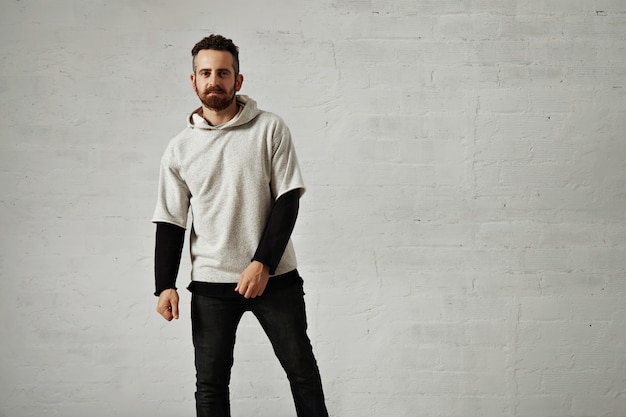Leeres hellgraues Sweatshirt, präsentiert von einem jungen Hipster mit einem Bartporträt mit weißen Wänden