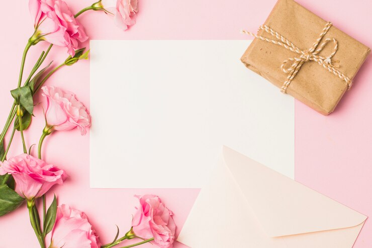 Kostenlose Foto leeres papier mit umschlag; frische rosa blume und braune eingewickelte geschenkbox über rosa hintergrund