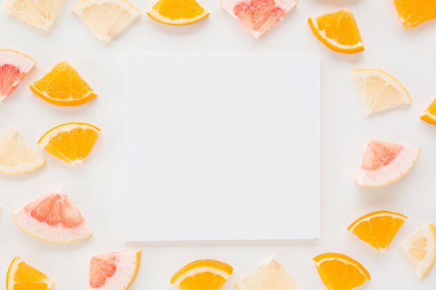 Leeres Papier umgeben mit bunten Zitrusfruchtscheiben auf weißem Hintergrund