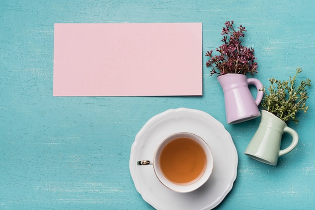 Leeres Papier und Vasen mit Tasse Tee auf blauem strukturiertem Hintergrund