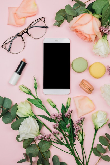 Leeres Smartphone; Brille; Lippenstift ; Rose; Limonium und Eustoma Blumen auf rosa Hintergrund