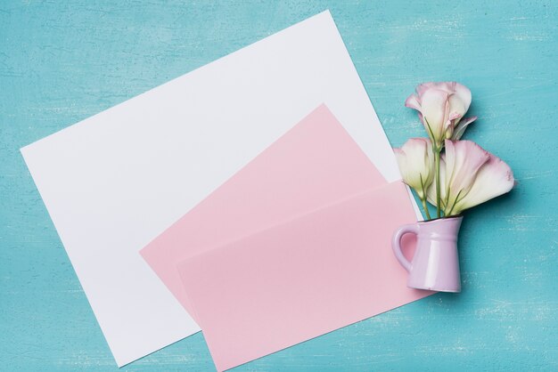 Leeres weißes und rosa Papier mit Eustomavase gegen blauen Hintergrund