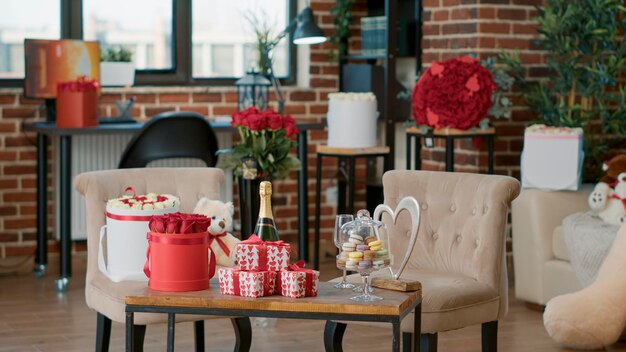Leeres Wohnzimmer, das von einem Freund mit romantischen Geschenken zum Valentinstag dekoriert wurde, damit die Freundin zu Hause ein romantisches Jubiläum feiern kann. Wohnzimmer mit roten Rosen auf dem Tisch. Konzept des Valentinsgeschenks