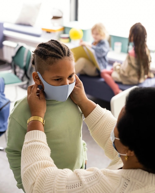 Lehrer, der einem Schüler hilft, eine medizinische Maske aufzusetzen