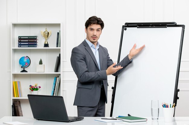 Lehrer intelligenter Lehrer im grauen Anzug im Klassenzimmer mit Computer und Whiteboard, der Mathematik erklärt