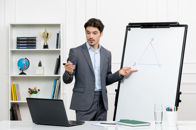 Lehrer junger Ausbilder im Büroanzug in der Klasse mit Computer und Whiteboard, der Mathematik erklärt