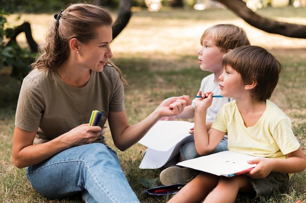 Lehrer und Kinder sitzen auf Gras mittlerer Schuss