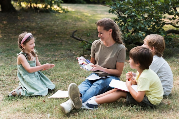 Lehrer und Kinder sitzen auf Gras