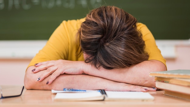 Lehrerin am Schreibtisch mit Kopf auf Deks