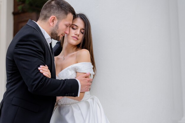 Leidenschaftliches Paar in Hochzeitskleidung steht nahe der weißen Wand, Ehekonzept