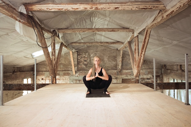 Leistung. Eine junge sportliche Frau übt Yoga auf einem verlassenen Baugebäude aus. Gleichgewicht der geistigen und körperlichen Gesundheit. Konzept von gesundem Lebensstil, Sport, Aktivität, Gewichtsverlust, Konzentration.