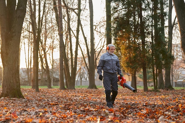 Kostenloses Foto leitender städtischer arbeiter geht mit laubbläser, um den stadtparkbereich zu säubern, vorderansicht konzentriert