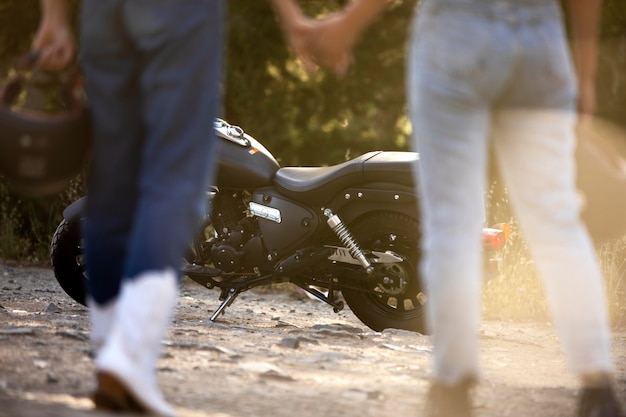 Lesbisches Paar Händchen haltend in der Nähe von Motorrad während eines Roadtrips