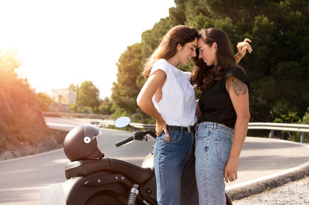 Lesbisches Paar umarmt sich während eines Roadtrips in der Nähe eines Motorrads