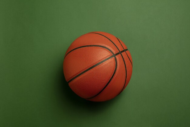 Leuchtender orange-brauner Basketballball. Professionelle Sportausrüstung lokalisiert auf grünem Hintergrund.