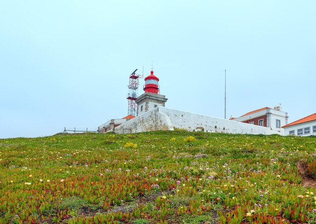 Leuchtturm am sommer blühenden cape roca (cabo da roca) mit blumen. blick auf die atlantikküste bei bewölktem wetter, portugal.