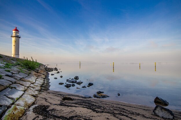 Leuchtturm am Ufer in der Nähe des Meeres mit einem blauen bewölkten Himmel