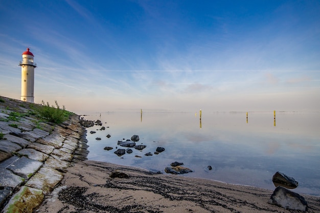 Leuchtturm am Ufer in der Nähe des Meeres mit einem blauen bewölkten Himmel